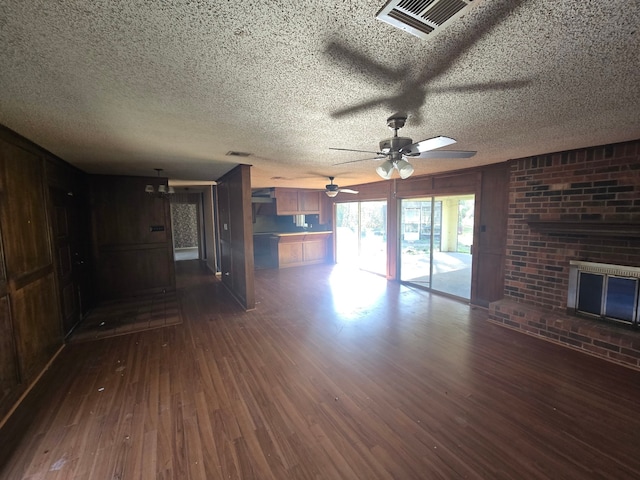 unfurnished living room featuring dark hardwood / wood-style flooring, a brick fireplace, a textured ceiling, ceiling fan, and wood walls