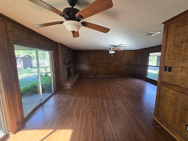 unfurnished living room featuring wood walls, a brick fireplace, ceiling fan, a textured ceiling, and dark hardwood / wood-style flooring