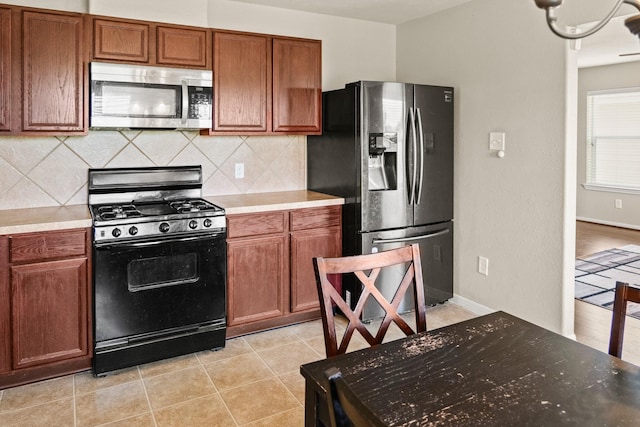 kitchen featuring backsplash, stainless steel appliances, an inviting chandelier, and light tile patterned flooring