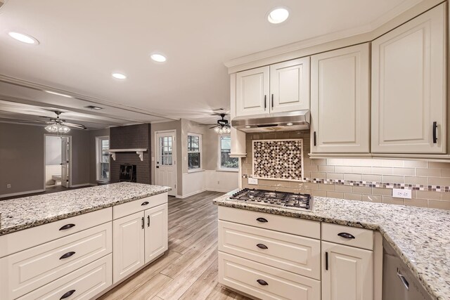 kitchen featuring light stone countertops, tasteful backsplash, stainless steel gas cooktop, ceiling fan, and light hardwood / wood-style flooring