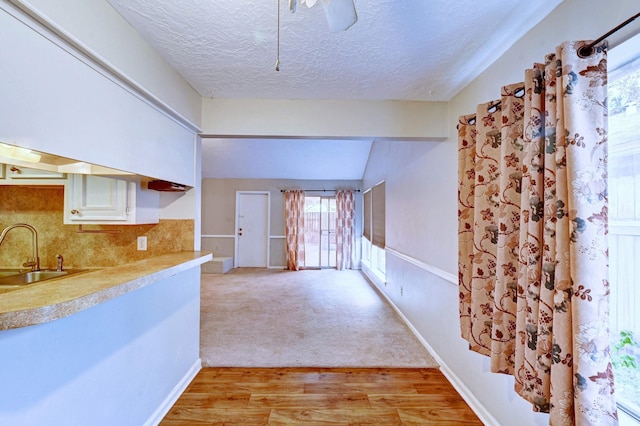 kitchen featuring sink, vaulted ceiling, a textured ceiling, tasteful backsplash, and light hardwood / wood-style floors