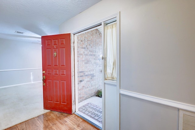 entrance foyer featuring a textured ceiling, brick wall, and light hardwood / wood-style flooring