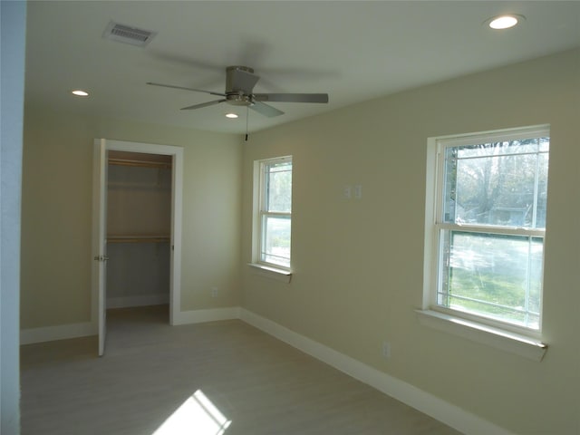 unfurnished bedroom with multiple windows, a closet, a spacious closet, and ceiling fan