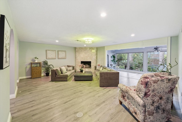 living room with a high end fireplace, light hardwood / wood-style flooring, and ceiling fan