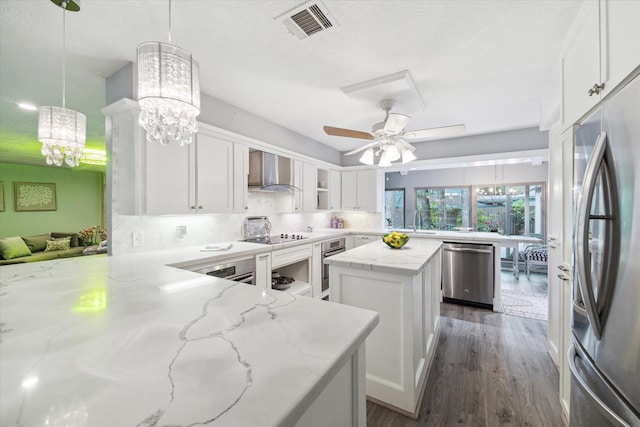 kitchen with a center island, white cabinets, hanging light fixtures, wall chimney exhaust hood, and appliances with stainless steel finishes