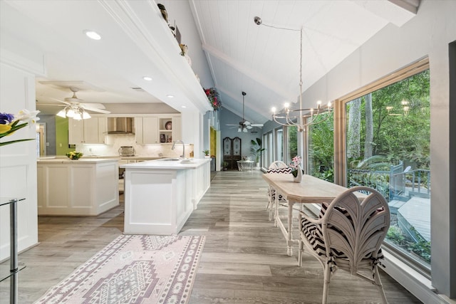 kitchen with wall chimney range hood, backsplash, pendant lighting, lofted ceiling, and light hardwood / wood-style floors