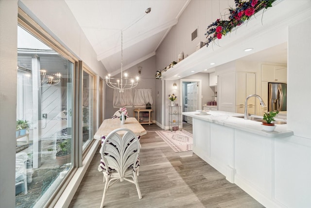 dining room featuring sink, wood-type flooring, plenty of natural light, and an inviting chandelier