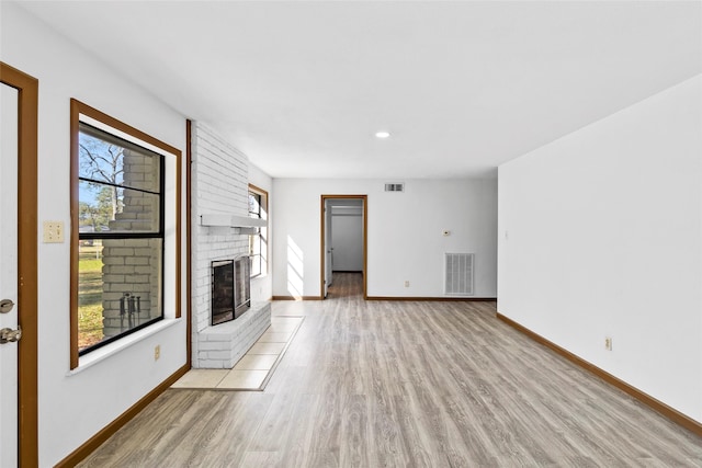 unfurnished living room featuring plenty of natural light, light wood-type flooring, and a brick fireplace