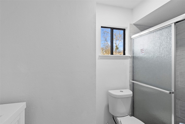 bathroom featuring a shower with door and toilet