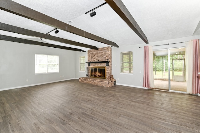 unfurnished living room with dark hardwood / wood-style floors, plenty of natural light, a textured ceiling, and a brick fireplace