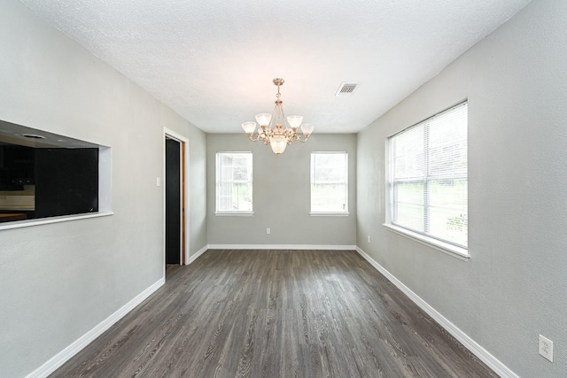 empty room featuring a chandelier, dark hardwood / wood-style flooring, a textured ceiling, and plenty of natural light