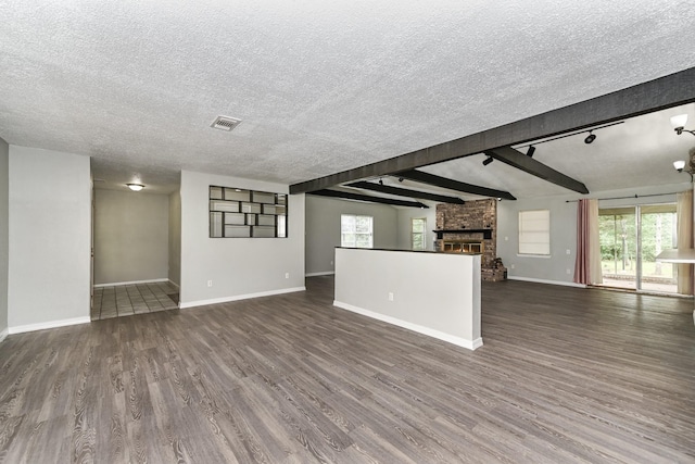 unfurnished living room featuring beam ceiling, rail lighting, dark hardwood / wood-style floors, a textured ceiling, and a fireplace