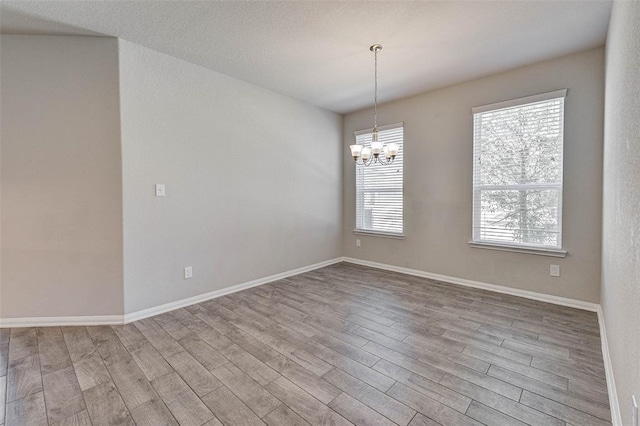 spare room with a chandelier and light wood-type flooring