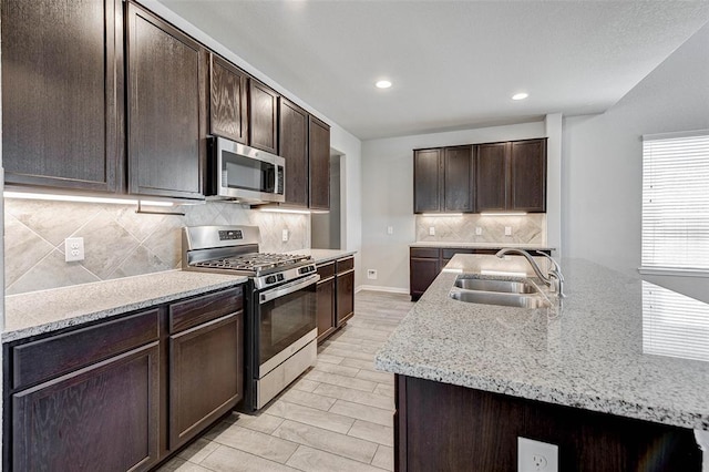 kitchen featuring dark brown cabinetry, stainless steel appliances, light stone counters, and sink