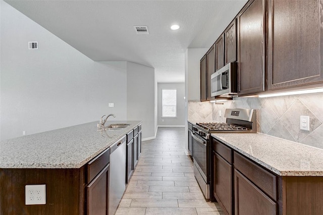 kitchen featuring a center island with sink, sink, light stone countertops, and stainless steel appliances