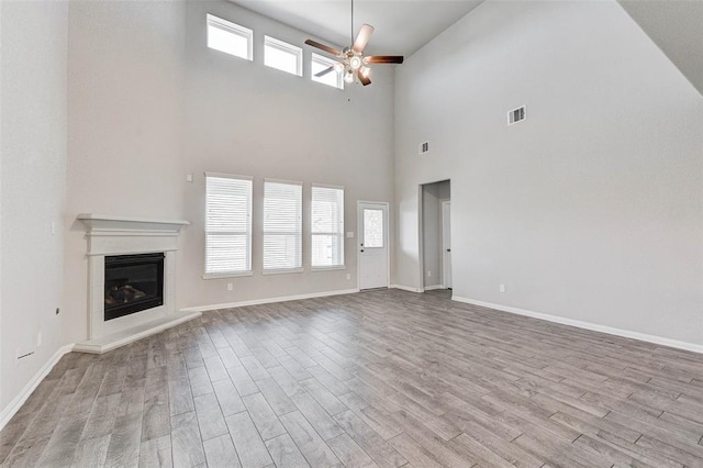 unfurnished living room with ceiling fan, light hardwood / wood-style floors, and a high ceiling