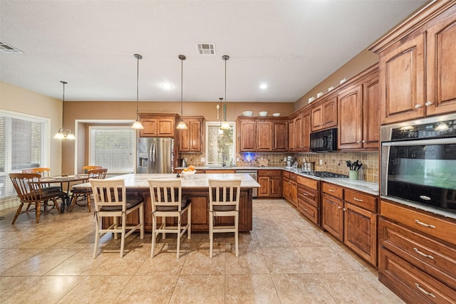 kitchen featuring decorative backsplash, appliances with stainless steel finishes, a kitchen breakfast bar, decorative light fixtures, and an island with sink