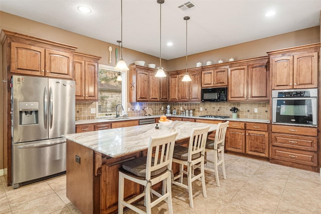 kitchen with appliances with stainless steel finishes, a kitchen breakfast bar, light stone counters, pendant lighting, and a kitchen island