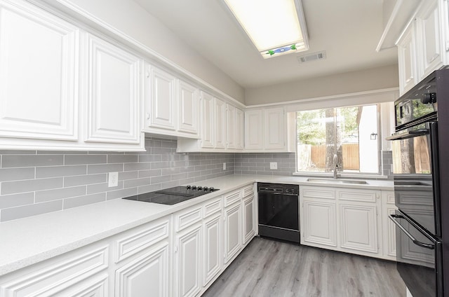 kitchen with tasteful backsplash, sink, black appliances, light hardwood / wood-style flooring, and white cabinets