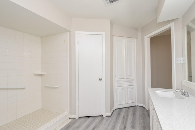 bathroom with tiled shower, vanity, and hardwood / wood-style flooring