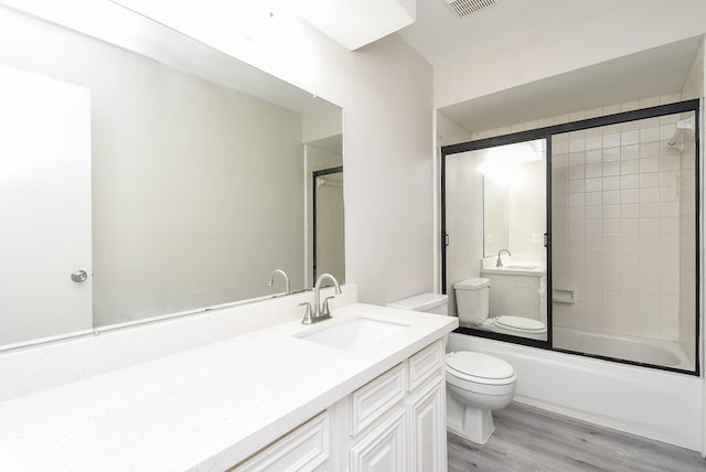 full bathroom with shower / bath combination with glass door, hardwood / wood-style floors, vanity, and toilet