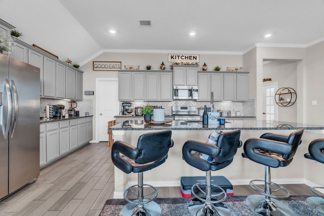 kitchen with ornamental molding, stainless steel appliances, lofted ceiling, and dark stone countertops