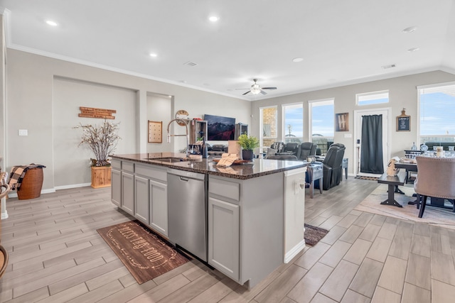 kitchen with dark stone counters, ceiling fan, sink, dishwasher, and an island with sink