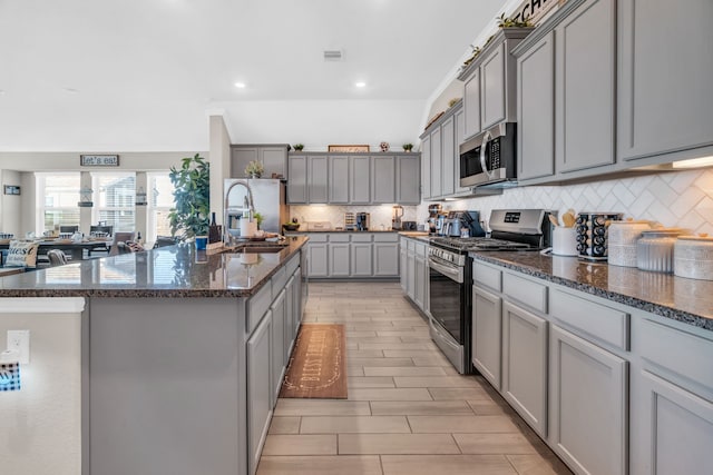 kitchen featuring gray cabinetry, sink, stainless steel appliances, and an island with sink