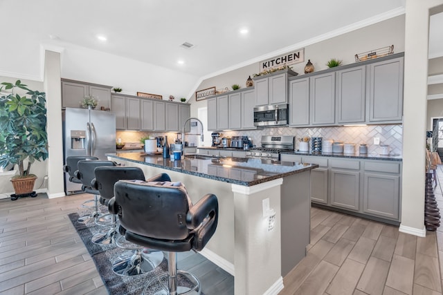 kitchen featuring dark stone counters, a center island with sink, sink, vaulted ceiling, and appliances with stainless steel finishes