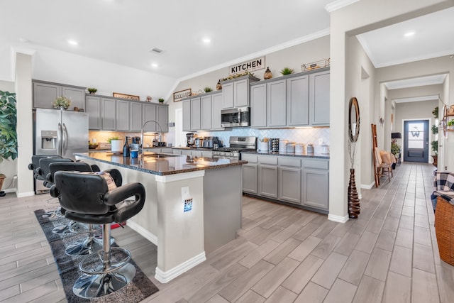 kitchen featuring a kitchen island with sink, dark stone counters, sink, appliances with stainless steel finishes, and a breakfast bar area