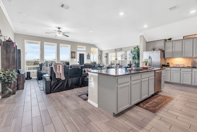 kitchen featuring appliances with stainless steel finishes, tasteful backsplash, ceiling fan, a center island with sink, and gray cabinets