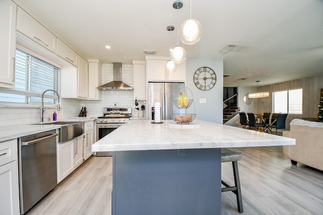 kitchen with a center island, white cabinetry, wall chimney range hood, and appliances with stainless steel finishes