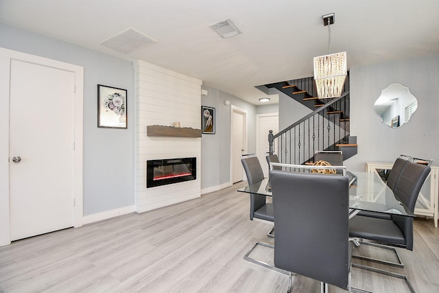 dining space featuring a large fireplace, a notable chandelier, and light hardwood / wood-style flooring