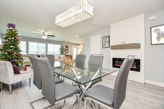 dining area featuring a large fireplace, light hardwood / wood-style flooring, and ceiling fan