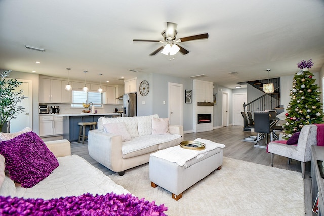 living room featuring ceiling fan, sink, light wood-type flooring, and a fireplace