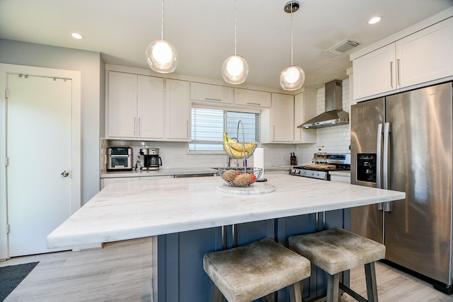 kitchen featuring white cabinets, stainless steel appliances, a kitchen island, and wall chimney range hood