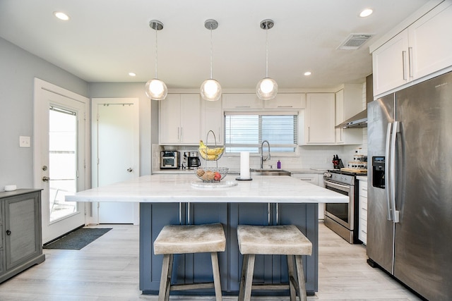 kitchen featuring appliances with stainless steel finishes, sink, wall chimney range hood, pendant lighting, and white cabinets