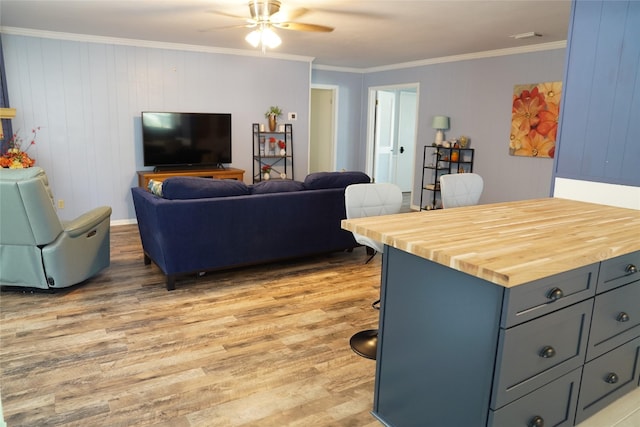 living room featuring crown molding, wooden walls, ceiling fan, and light wood-type flooring