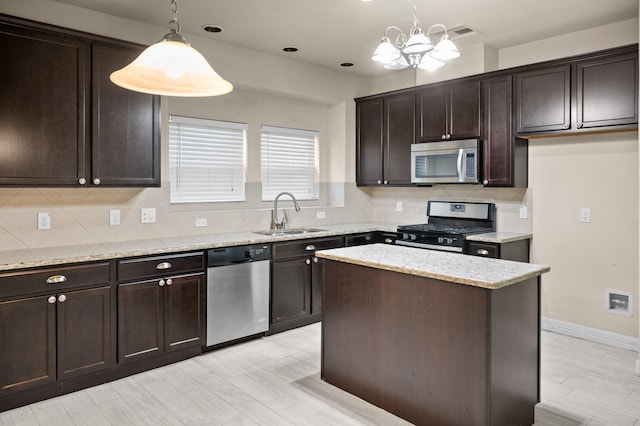 kitchen featuring sink, appliances with stainless steel finishes, decorative light fixtures, a kitchen island, and light wood-type flooring