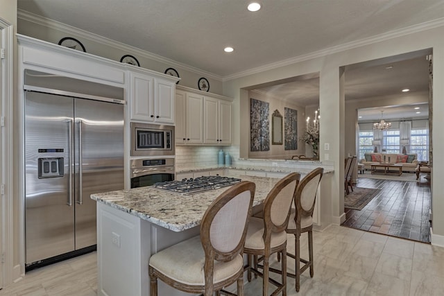 kitchen featuring light stone countertops, a kitchen breakfast bar, a notable chandelier, backsplash, and built in appliances