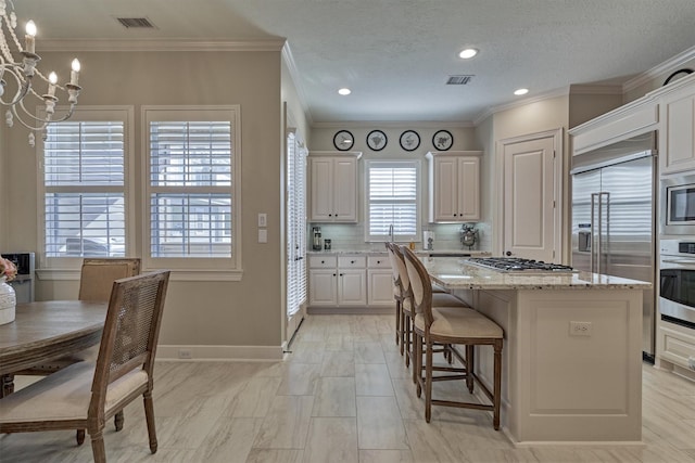 kitchen with tasteful backsplash, built in appliances, a notable chandelier, a center island, and white cabinetry