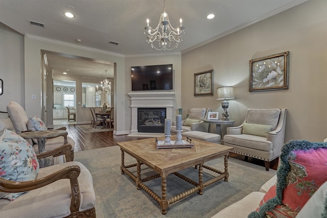 living room with a tiled fireplace, crown molding, an inviting chandelier, and hardwood / wood-style flooring