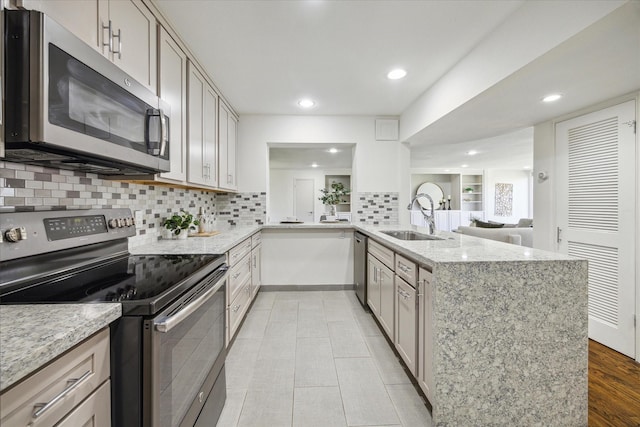 kitchen with backsplash, sink, light stone counters, kitchen peninsula, and stainless steel appliances