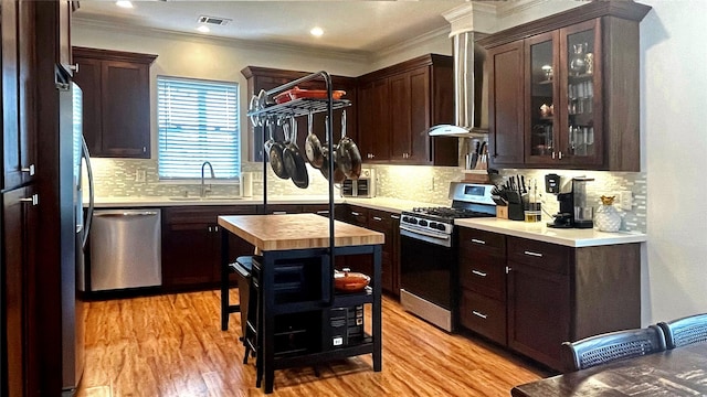 kitchen featuring dark brown cabinetry, sink, stainless steel appliances, wall chimney range hood, and wooden counters