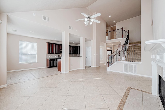 unfurnished living room featuring light tile patterned floors, high vaulted ceiling, ceiling fan, and a premium fireplace