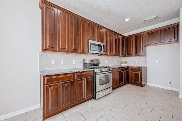 kitchen with light stone countertops, stainless steel appliances, backsplash, a textured ceiling, and light tile patterned floors