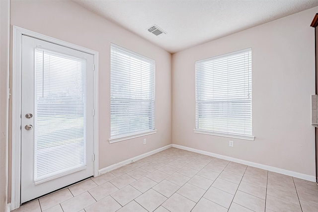 tiled empty room featuring a wealth of natural light and a textured ceiling