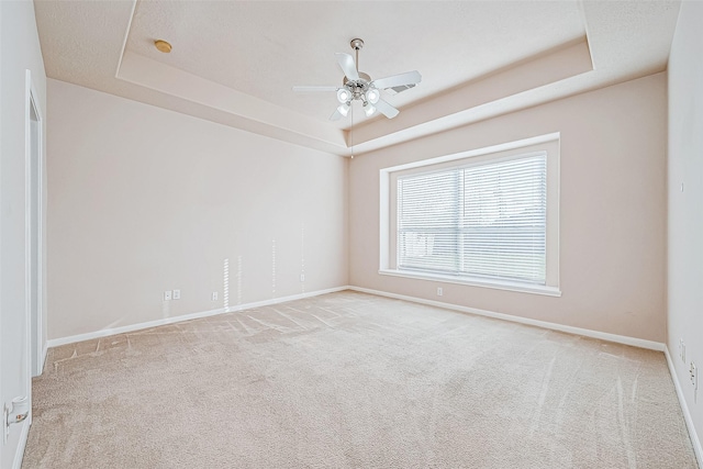 empty room with ceiling fan, light carpet, and a tray ceiling