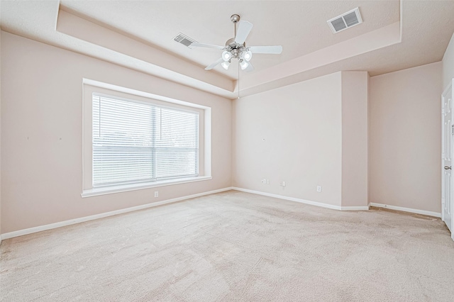 empty room with ceiling fan, light colored carpet, and a tray ceiling