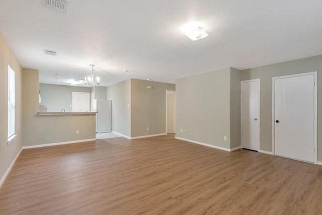 unfurnished room with a notable chandelier and light wood-type flooring